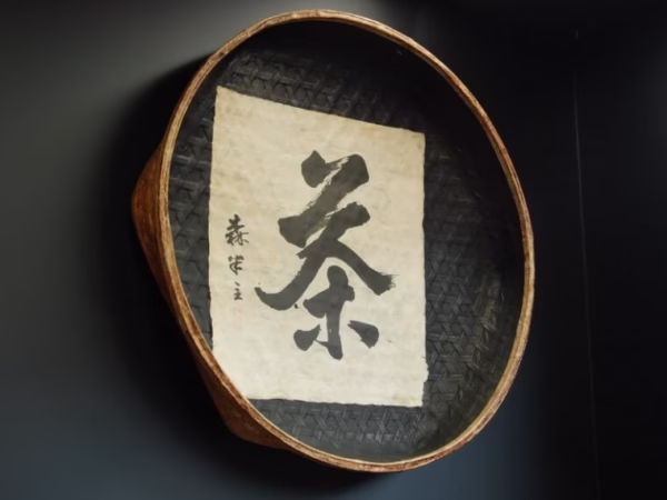 お茶を選別するときに用いるザルの内側に「茶」の文字が書かれている壁掛けの写真です。